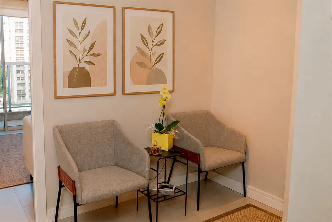 Recepção com duas poltronas cinza, quadros botânicos e orquídea amarela