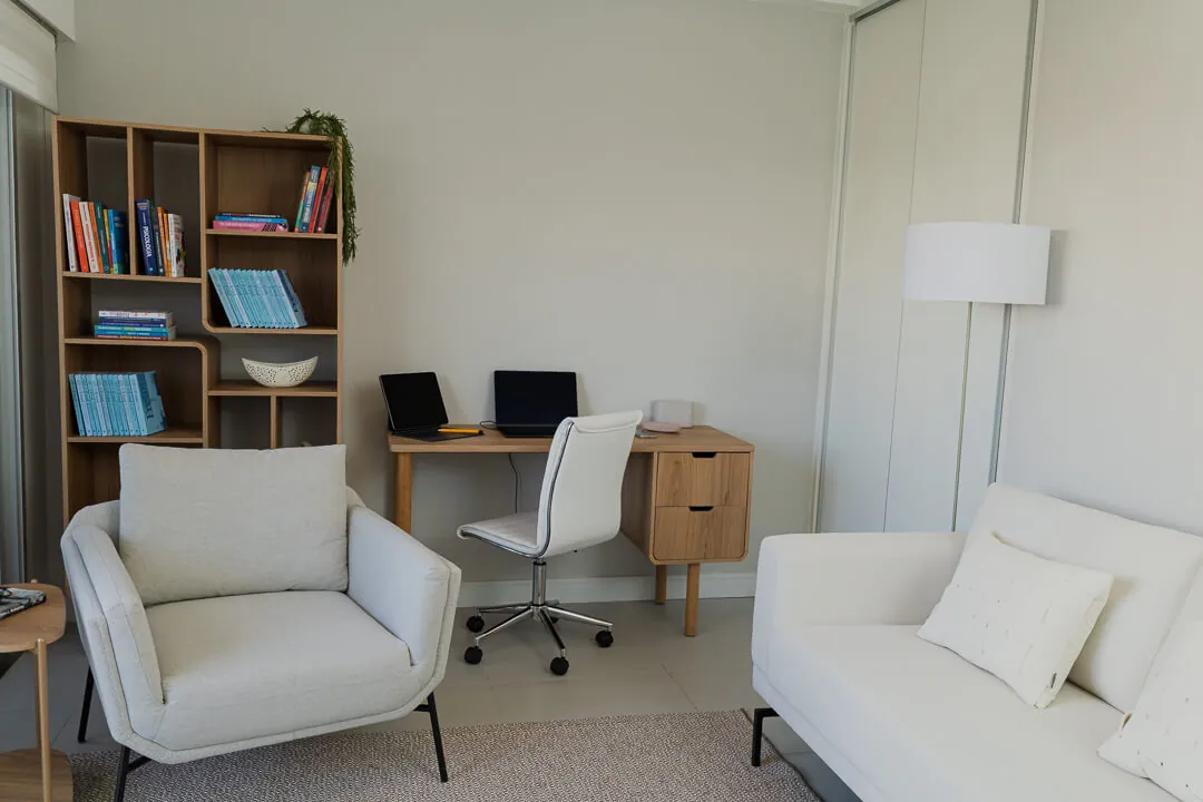 Sala de atendimento com poltrona, sofá, escrivaninha e estante de livros